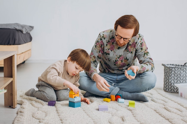 Pai de óculos e filho adorável criança construir torre de madeira do construtor.