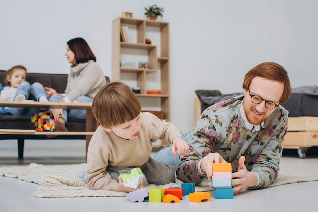 Pai de óculos e filho adorável criança construir torre de madeira do construtor.