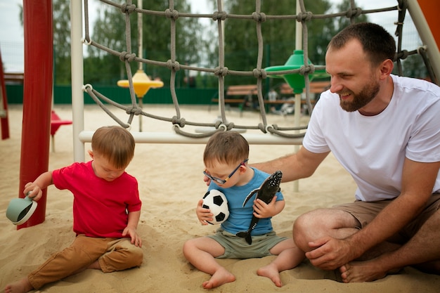Foto pai de vista frontal sentado na areia com filhos