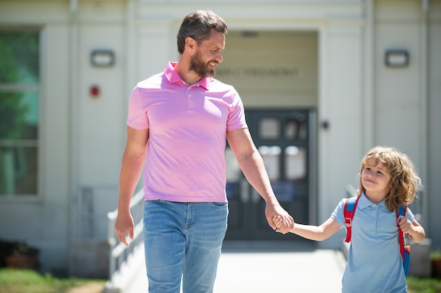 Pai e aluno da escola primária andam de mãos dadas professor de camiseta e estudante bonito com backpac
