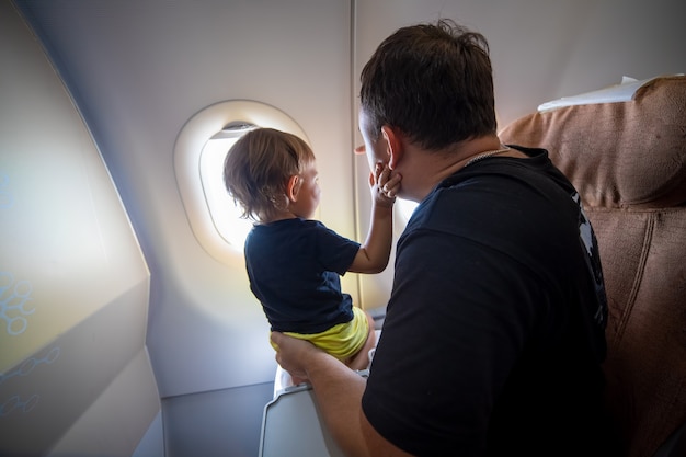 pai e criança bonita sentado em um avião e olhando para o céu pela vigia. primeiro conceito de voo, viajando com crianças