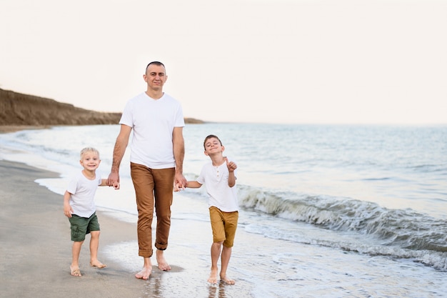 Pai e dois filhos caminham à beira-mar. curtindo férias