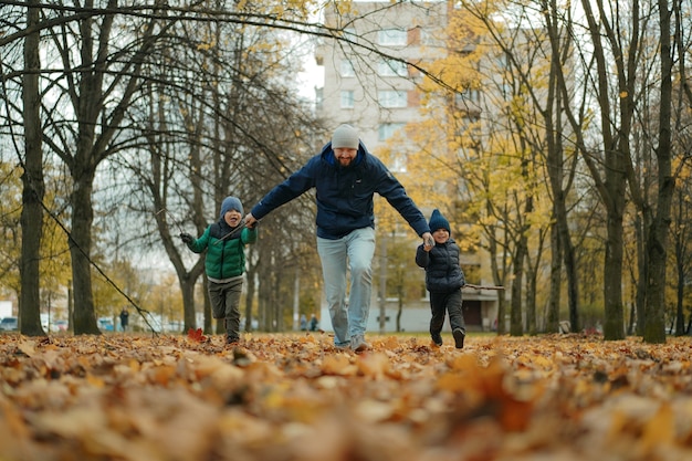 pai e dois filhos correndo pelo parque de outono de mãos dadas