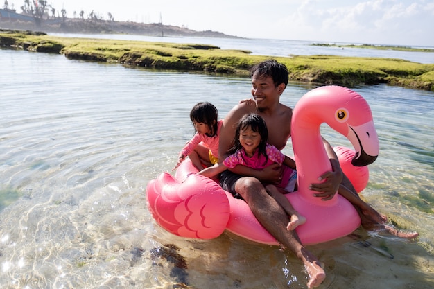 Pai e duas filhas montar bóia flamingo na praia