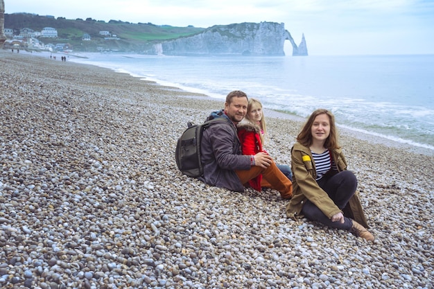 Pai e duas filhas sentadas na praia de Etretat