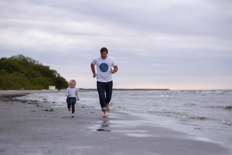 Foto pai e filha a brincar na praia contra o céu.