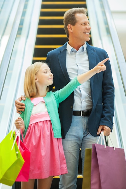 Pai e filha às compras. pai e filha alegres descendo pela escada rolante segurando sacolas de compras