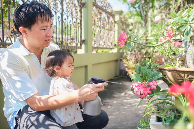 Pai e filha asiáticos se divertindo com um borrifador regando plantas em casa em uma manhã ensolarada