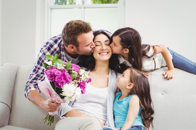 Pai e filha beijando mãe sentada no sofá