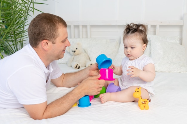 Pai e filha brincam com brinquedos coloridos na cama em casa em um quarto bem iluminado