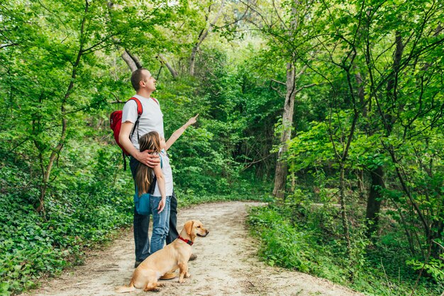 Pai e filha caminhando pela floresta com cachorro