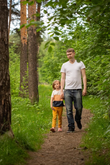 Pai e filha caucasiana caminham na floresta no verão, a garota segura a mão do pai