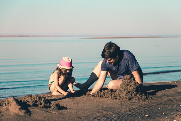 Pai e filha constroem castelos de areia na praia. Foto de estilo de vida tonificada.