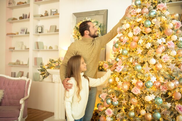 Pai e filha decorando a árvore de Natal e parecendo envolvidos