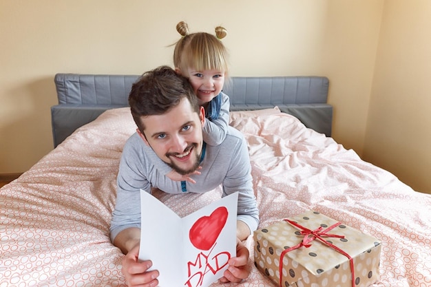 Pai e filha deitam na cama em um dia ensolarado