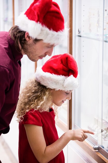 Pai e filha em trajes de natal, olhando para a exibição de jóias