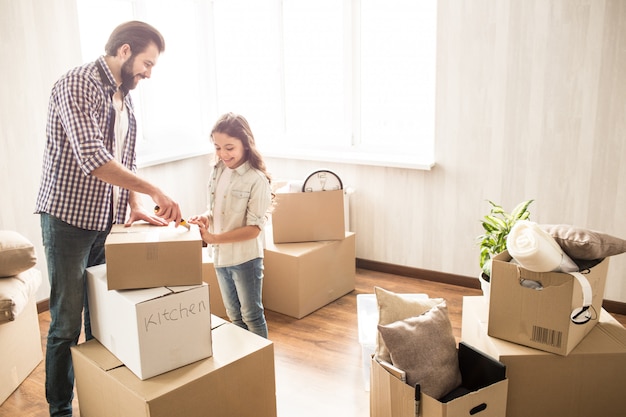 Pai e filha estão descompactando caixas juntos. eles têm muito trabalho a fazer. eles estão sem a mãe agora. esse povo parece feliz e satisfeito.