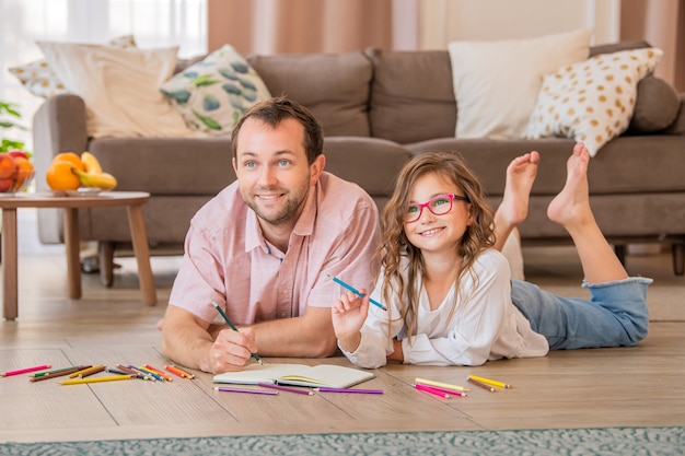 Pai e filha estão desenhando juntos enquanto estavam deitados no chão no quarto do apartamento.