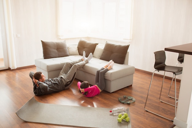 Pai e filha estão fazendo abdominais em casa. treino no apartamento.