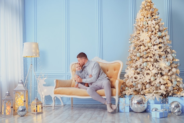 Pai e filha estão sentados em um sofá perto da árvore de Natal. Sessão de fotos de Natal.