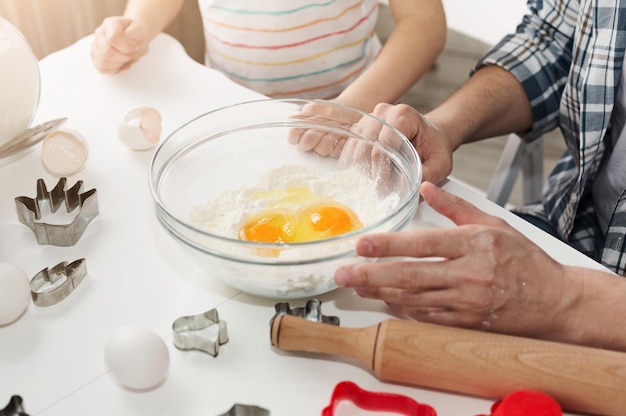 Pai e filha fazendo biscoitos. Filho e pai mãos na mesa com tigela de ovos e formas. Fim de semana em família, conceito culinário e de panificação, closeup.