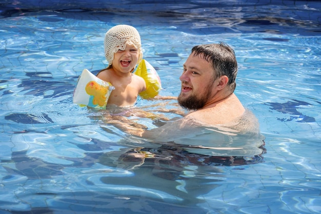 Foto pai e filha felizes a rir-se na piscina.