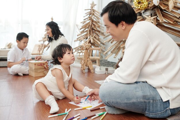 Pai e filha felizes desenhando fotos de natal no chão