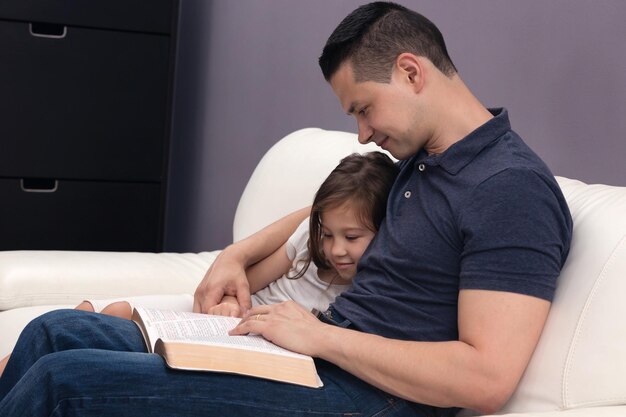 Foto pai e filha lendo livro no sofá em casa