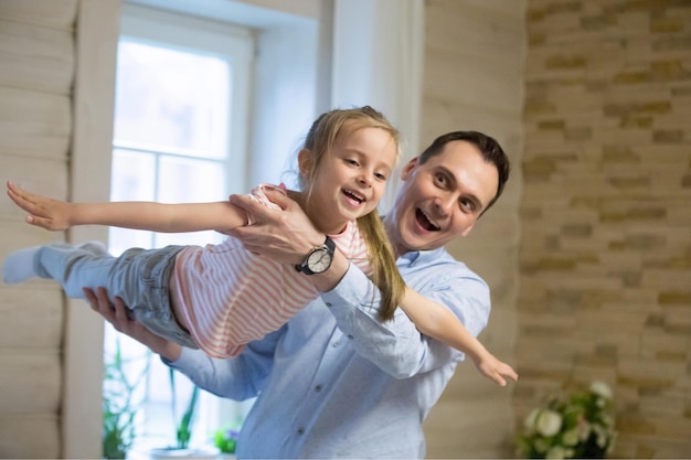 Pai e filha muito felizes brincando no fim de semana em casa Garotinha feliz voando como um avião no ar nas mãos do papai passando um tempo juntos rindo sorrindo Paternidade família conceito de tempo de lazer