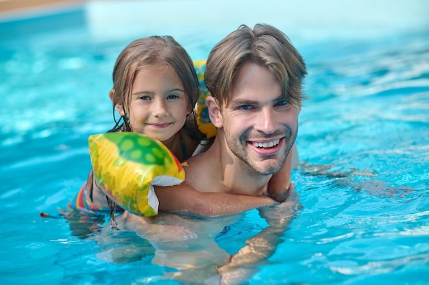 Pai e filha nadando juntos em uma piscina