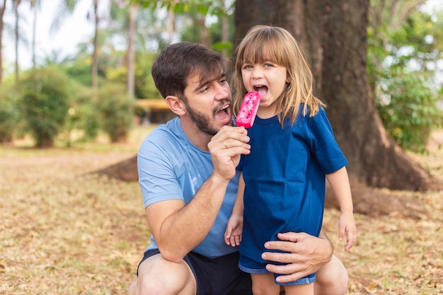 Pai e filha no parque chupando um delicioso picolé