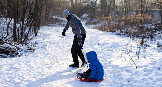 Pai e filha novos na neve com trenó.