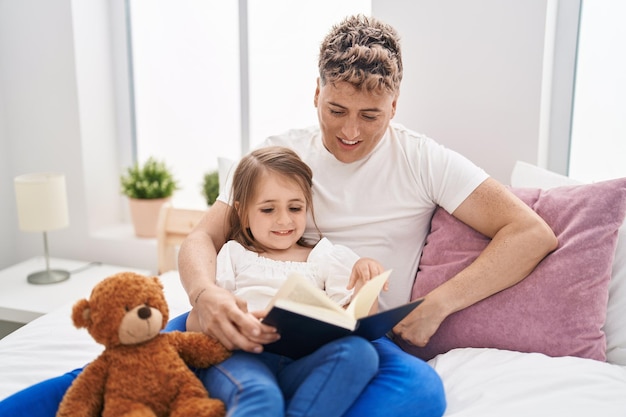 Pai e filha pai e filha lendo livro segurando ursinho de pelúcia no quarto