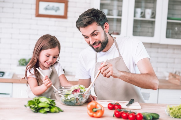 Pai e filha preparando salada na cozinha juntos