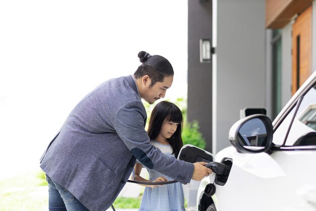 Pai e filha progressivos carregando carro EV da estação de carregamento em casa