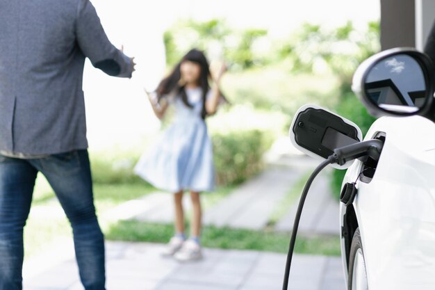 Pai e filha progressivos carregando carro EV da estação de carregamento em casa