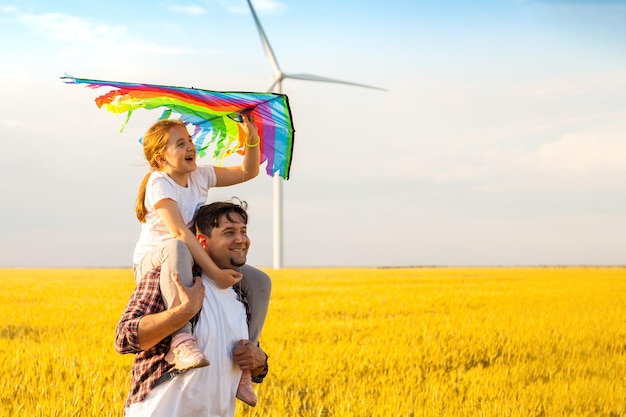 Pai e filha se divertindo brincando com pipa juntos no campo de trigo no dia de verão brilhante