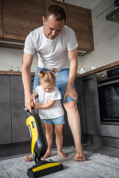 Pai e filha se divertindo com aspirador de pó enquanto limpam a cozinha de casa