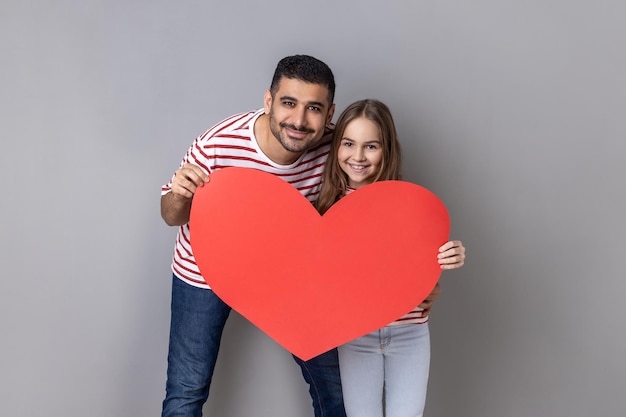 Pai e filha segurando um grande vermelho ouvem olhando para a câmera expressando amor um pelo outro