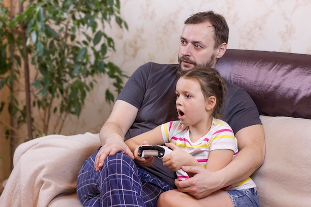 Pai e filha sentados no sofá em casa e jogando videogame