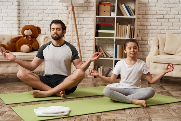 Pai e filha sentam-se em lotus pose no tapete.