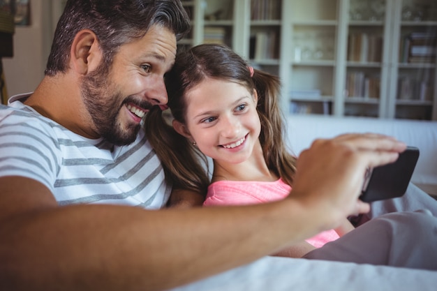 Pai e filha sorrindo, olhando para o telefone móvel na sala de estar