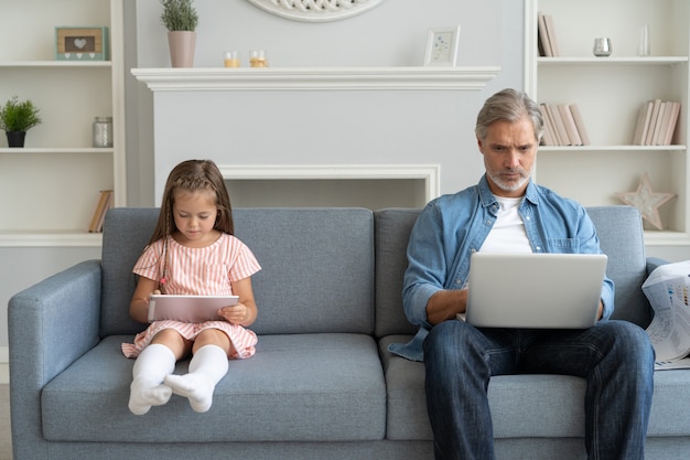 Pai e filha usando dispositivos eletrônicos em casa.