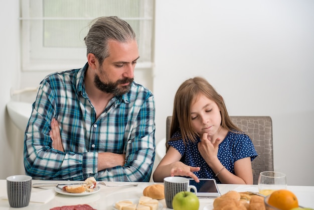 Pai e filha usando tablet durante café da manhã