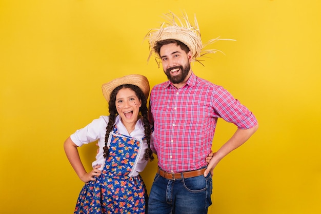 Foto pai e filha vestindo roupas típicas da festa junina com a mão na cintura para a festa do arraia