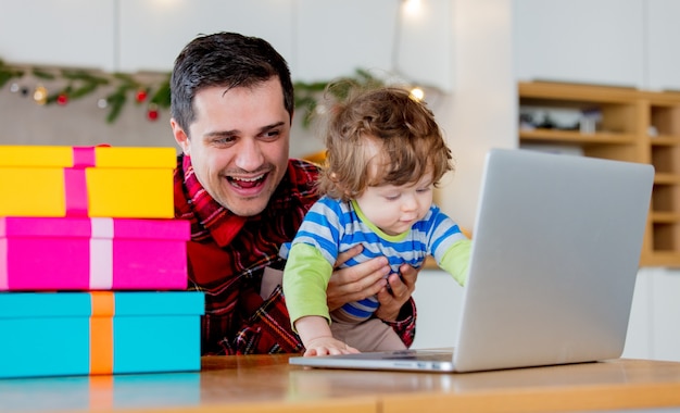 Pai e filho à procura de presentes de natal no computador portátil, sentado na cozinha em casa.