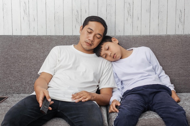 Pai e filho adormecem ao assistir televisão no sofá vestindo camiseta branca adequada