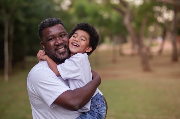 Pai e filho afro, abraçados no parque. Dia dos Pais.