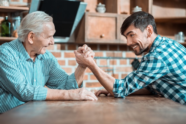 Pai e filho alegres e encantados, olhando um para o outro e lutando contra a queda de braço enquanto se divertem juntos