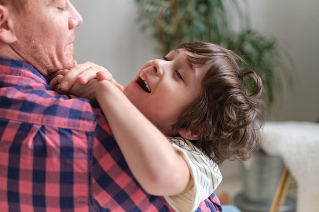 Pai e filho alegres se unem por meio de cócegas lúdicas, criando uma atmosfera calorosa e feliz no quarto